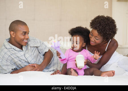 Happy parents and baby girl sitting on bed together Stock Photo