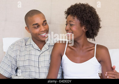 Happy couple sitting on bed smiling at each other Stock Photo