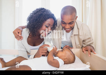 Happy parents feeding their baby boy in his crib Stock Photo