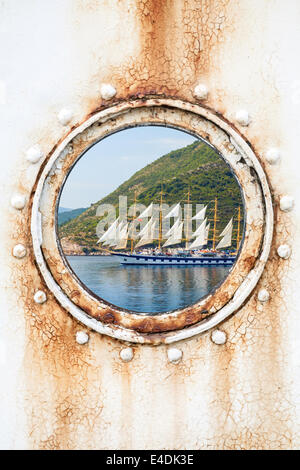 Big sailing ship behind round rusted porthole on white wall Stock Photo