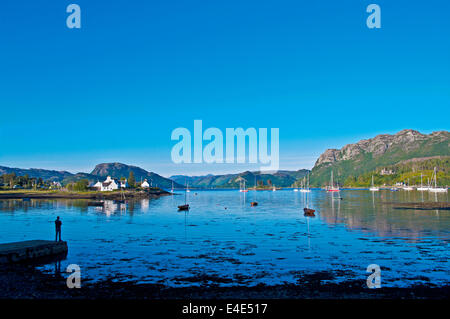 Man standing on jetty looking over boats moored in Plockton harbour, calm summer evening, Loch Carron, Wester Ross, Scotland UK Stock Photo
