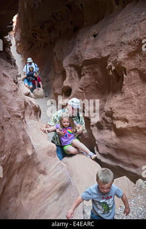 Hanksville, Utah - Adults help children over obstacles while hiking in Little Wild Horse Canyon. Stock Photo