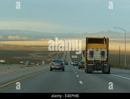 A long road through America leading towards last Vegas in the distance with cars and a truck in the foreground Stock Photo