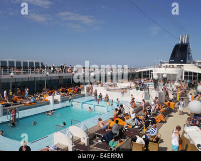 The top deck of a busy cruise ship with people sitting around the pool on a sunny day Stock Photo