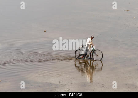 AGRA, INDIA - MARCH 2014: Indian man walks his bicycle across Yamuna river in Agra in March 2014. Stock Photo