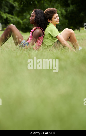 Interracial people in love with black little girl caucasian and boy, leaning back to back on grass in park Stock Photo
