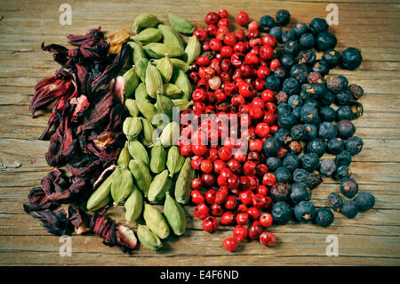 a pile of dried hibiscus flowers, green cardamom, pink peppercorns and juniper berries on a rustic wooden table Stock Photo