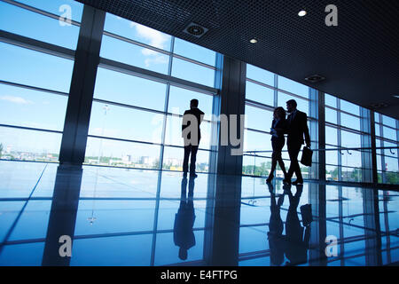 Silhouettes of office worker standing by the window and two business partners communicating while walking near by Stock Photo