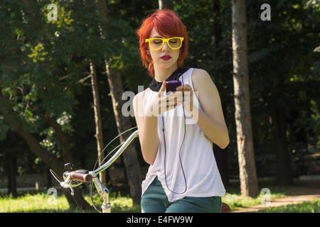 Hipster teenage girl on her vintage bike, listening to the music on her purple smart phone Stock Photo
