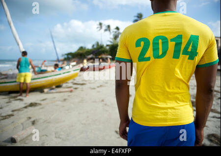 Brazilian football player in 2014 shirt colors standing in front of fishing boats on Nordeste Brazil beach Stock Photo