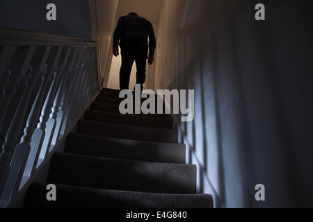 Silhouette of a man walking upstairs back view, shadows cast on the walls from the light below. Stock Photo