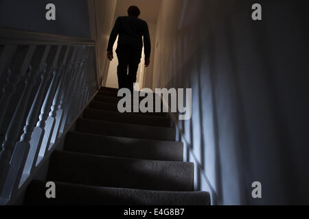 Silhouette of a man walking upstairs back view, shadows cast on the walls from the light below. Stock Photo