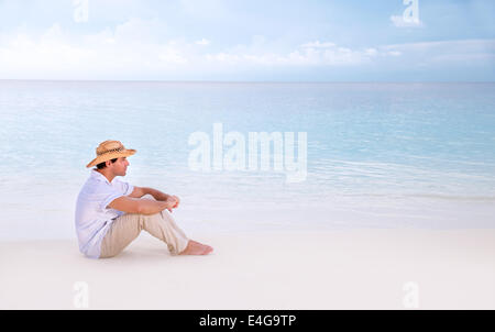 Thoughtful man sitting on the beach, side view, looking away, relaxation near sea, enjoying seascape, summer holidays Stock Photo
