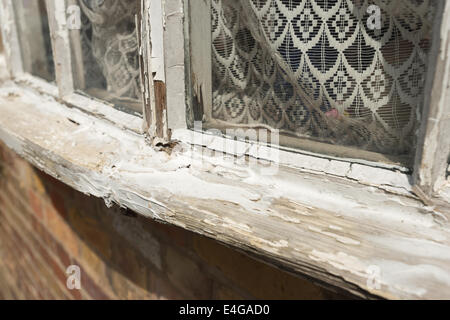 What lays hidden inside behind this laced curtain glass pane with deteriorating painted wooden window sill needing renovation Stock Photo