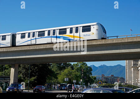 The Skytrain elevated light rapid transit system train crossing over a busy street, Vancouver, BC, Canada Stock Photo