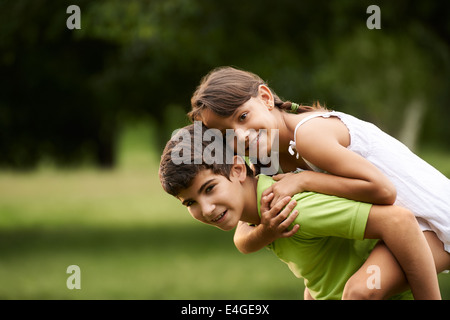 People in love with happy little girl and boy running piggyback in city park. Copy space Stock Photo