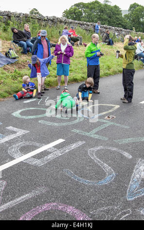 Children chalking riders names on the road before the arrival of the Tour De France near Hawes, North Yorkshire, England, UK Stock Photo