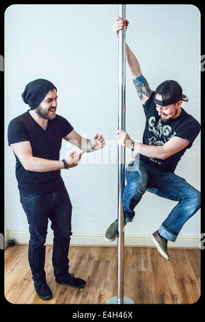 Two young men playing on a sports pole, learning how to pole dance Stock Photo