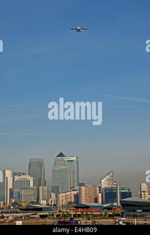 An aircraft heading towards London City airport passes over the skyscrapers of Canary Wharf in East London, with air pollution visible in the sky Stock Photo