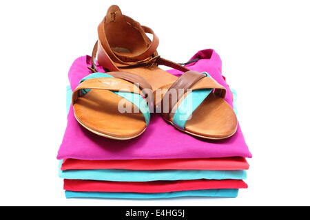Leather sandals lying on pile of colorful shirts. Isolated on white background Stock Photo