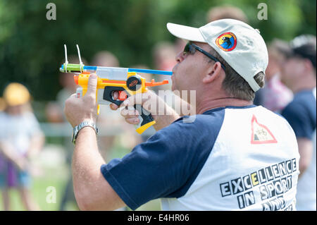 Witcham near Ely Cambridgeshire UK 12th July 2014. A competitor takes part in the 44th World Pea Shooting Championships. The quirky event has been running since 1971 and raises funds for the village hall. The peashooter may be made of any material but must not exceed 12 inches in length and may include sighting devices.  Peashooters vary from plain tubes to high-tech laser sighted devices.  Peas are fired at a putty target from a distance of 12 feet. Five peas are used in the qualifying  rounds and 10 for the finals. Credit Julian Eales/Alamy Live News Stock Photo