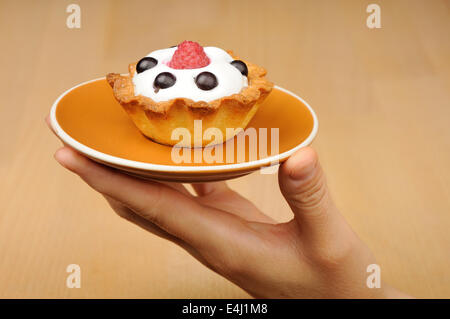 biscuit with cream, raspberry and currant on the plate in woman's hand