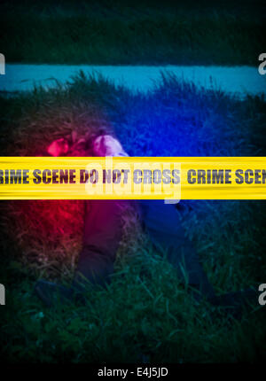 Yellow crime scene cordon tape over a blurred body of a man in the grass, unidentifiable person. Stock Photo