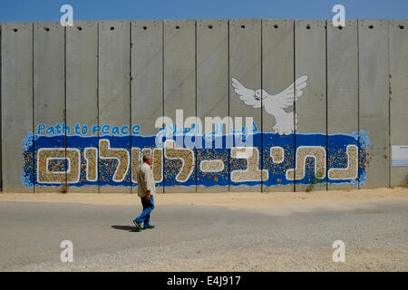 An Israeli civilian walks past a precast concrete wall decorated with joint mosaic which forms writing “Path to Peace” created by visitors who write a personal wish on the back of a colorful mosaic piece and glue it onto the defense wall, adjacent to the homes of the Israeli settlement  Moshav Netiv HaAsara facing northern Gaza Strip in Israel Stock Photo