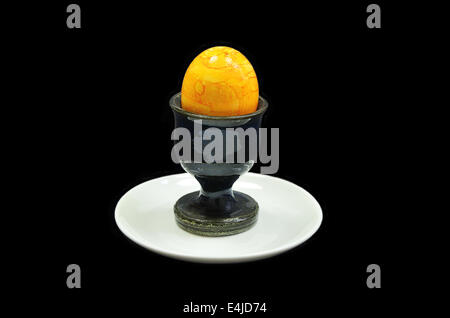 yellow hard boiled egg in an egg cup on white plate, close up, isolated on black background Stock Photo