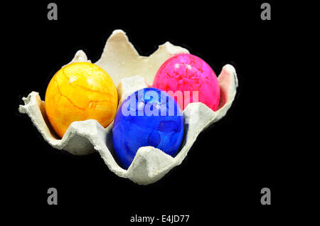 three colorful easter eggs in a cardboard box, close up, isolated on black background Stock Photo