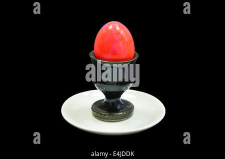 red hard boiled egg in an egg cup on white plate, close up, isolated on black background Stock Photo