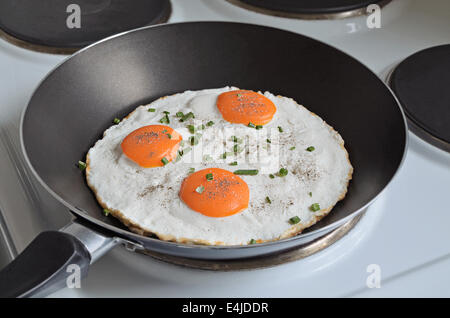 fried eggs with three yolks and chive in a frying pan, close up Stock Photo