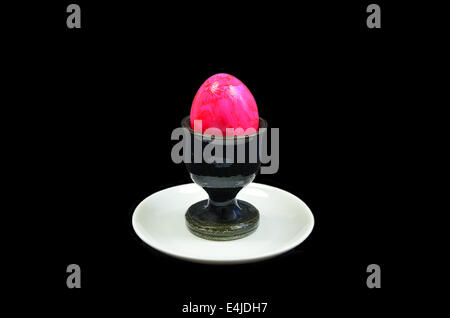 pink hard boiled egg in an egg cup on white plate, close up, isolated on black background Stock Photo