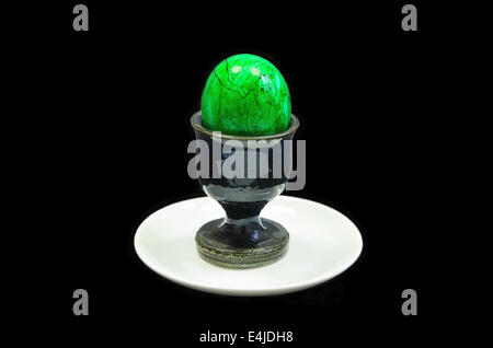 green hard boiled egg in an egg cup on white plate, close up, isolated on black background Stock Photo