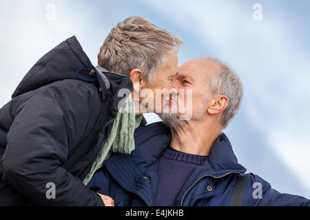 Elderly couple taking a self portrait on a compact digital camera posing in the open air and sunshine with their heads close tog Stock Photo