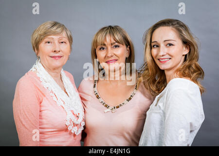 Three generations of attractive women with blond hair and a striking family resemblance posing together arm in arm looking at th Stock Photo