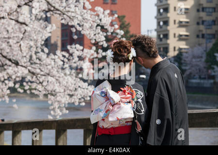 Young couple in traditional wedding attire on bridge in Higashi Chaya district during cherry blossom season, Kanazawa, Japan Stock Photo