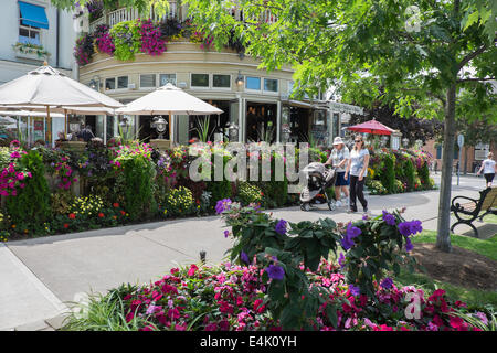 Tourists walk by one of many colourful floral displays which can be found in the historic old town of Niagara-on-the-Lake, Ontario, Canada. Stock Photo