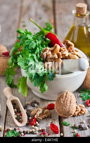 Cilantro, walnuts and red hot pepper in white ceramic mortar on wooden table Stock Photo