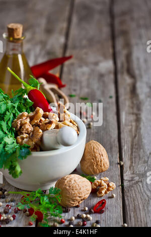 Cilantro, walnuts and red hot pepper in white ceramic mortar on wooden table. Copy space background. Stock Photo