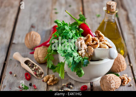 Cilantro, walnuts and red hot pepper in white ceramic mortar on wooden table Stock Photo