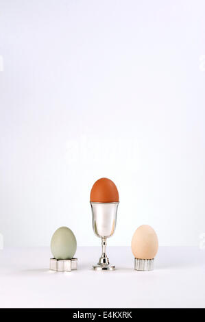 Three free range hens eggs in various colours and cups on a white background. Stock Photo