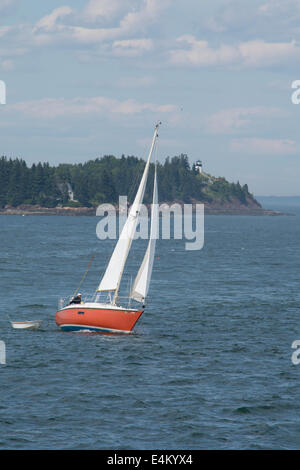 Maine, Rockland, Penobscot Bay. Red sailboat in front of Owls Head State Park, historic Owls Head Lighthouse, circa 1852. Stock Photo
