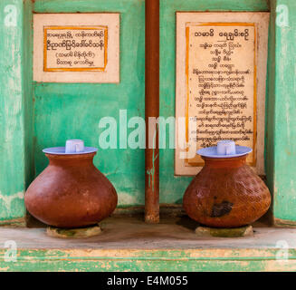 Two water pots with communal cups sit in a kiosk for monks and nuns at the  Maha Aung Mye Bonzan Monastery in Mandalay, Myanmar. Stock Photo