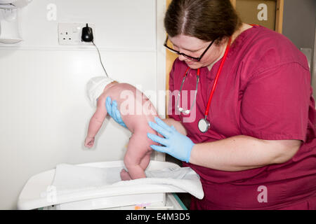 Midwife performs the Physical examination health check test test on newborn / new born baby after childbirth / being born. UK Stock Photo