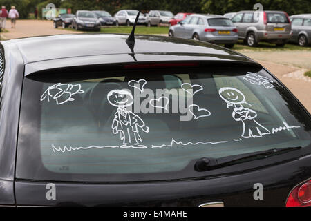 Figures of bride and groom painted on the rear window of a honeymooners' black car Stock Photo