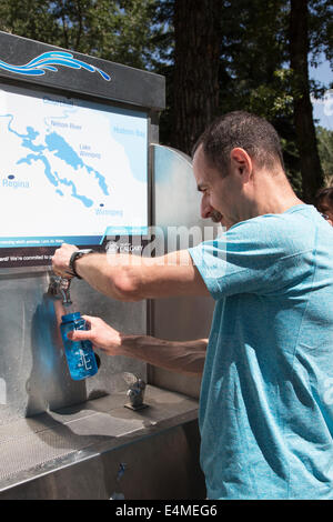 Man filling  his own reusable water bottle from H2O buggy (mobile water station) in city park Stock Photo