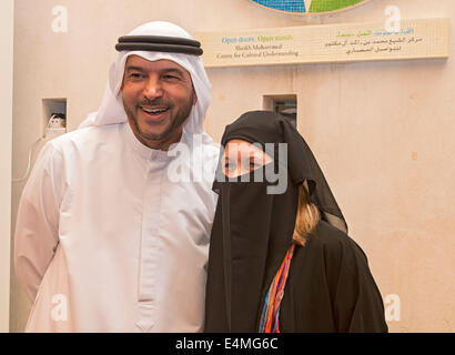 Muslim guide Nasif Kayed, in Arab robe and headdress, helps visiting American woman try on traditional abaya robe Stock Photo