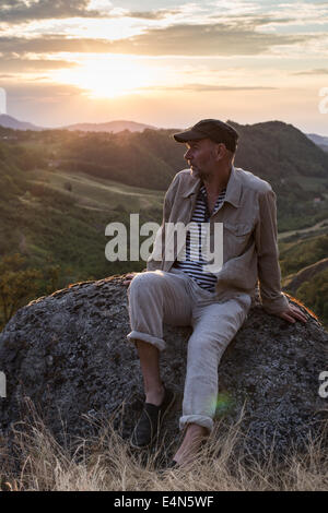 caucasian man sitting on rock in countryside on a hill looking into the distance Stock Photo