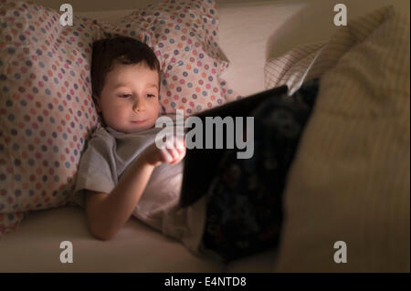 Boy (6-7) using digital tablet in bed Stock Photo